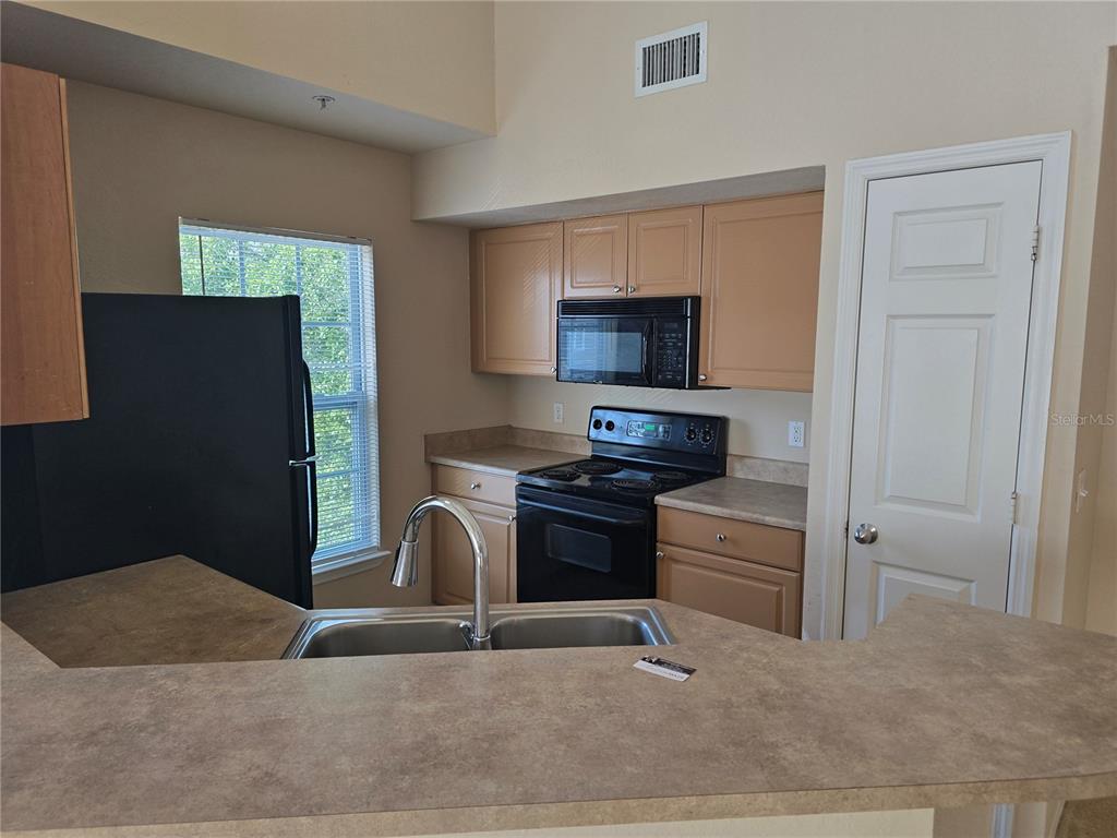 A kitchen features light wood cabinets, black appliances, a double sink, and laminate countertops — 5601 ROSEHILL ROAD UNIT 203, SARASOTA, FL