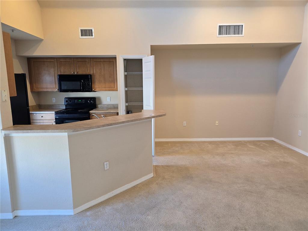 A kitchen with wood cabinets and black appliances overlooks a carpeted living area — 5601 ROSEHILL ROAD UNIT 203, SARASOTA, FL