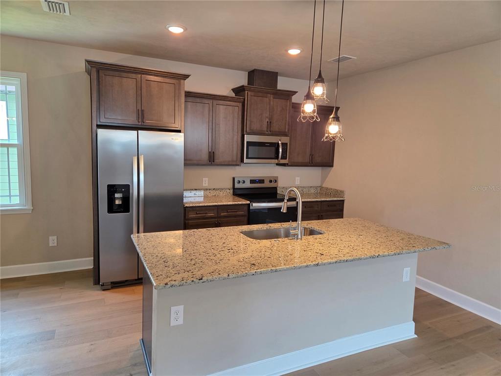 A kitchen features dark wood cabinets, granite countertops, stainless steel appliances, and a central island — 24313 SW 17TH LANE, NEWBERRY, FL
