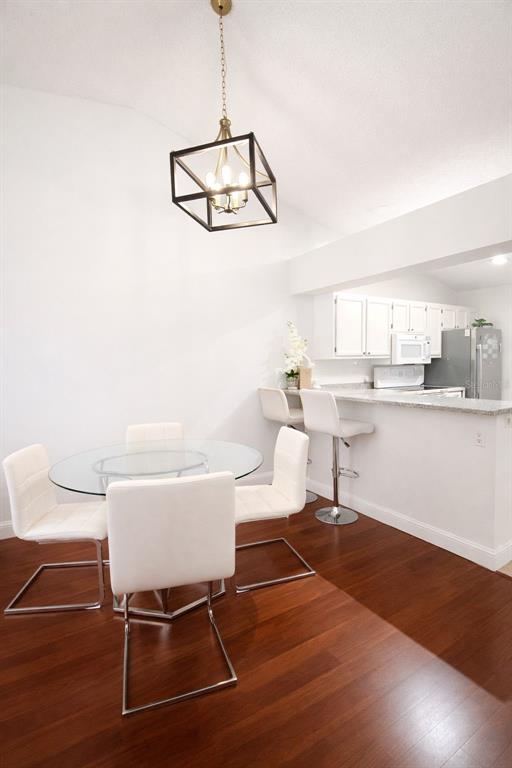 A dining area with a glass table, white chairs, and a breakfast bar with stools — 5473 LAKE MARGARET DRIVE UNIT G, ORLANDO, FL