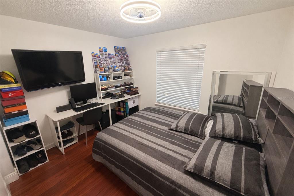 A bedroom features a bed with striped bedding, a desk, a television, and shelving units — 5473 LAKE MARGARET DRIVE UNIT G, ORLANDO, FL