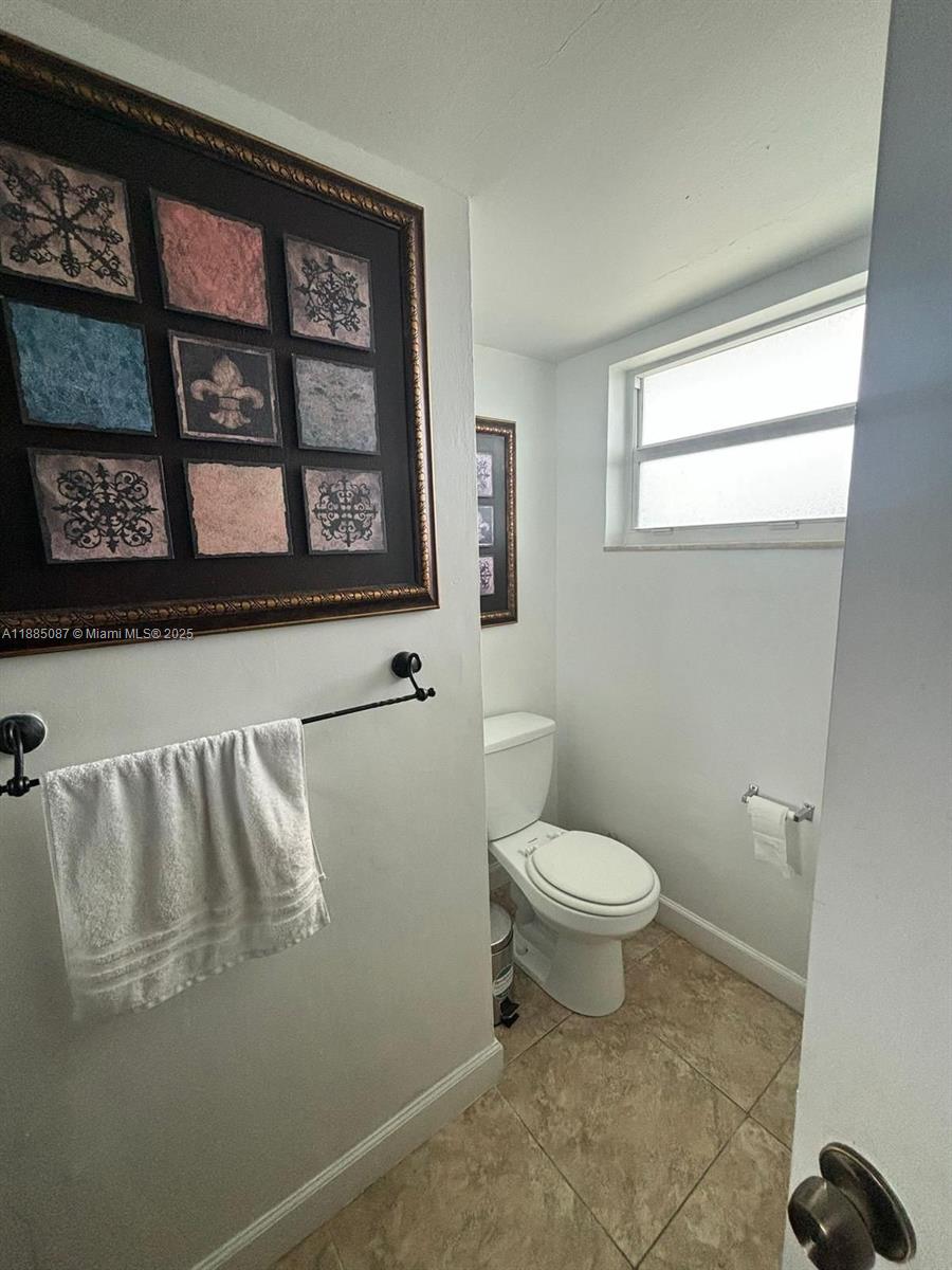A small bathroom features a white toilet, tiled flooring, and decorative wall art — 1780 NE 191st St # 2, Miami FL 33179, MIAMI, FL