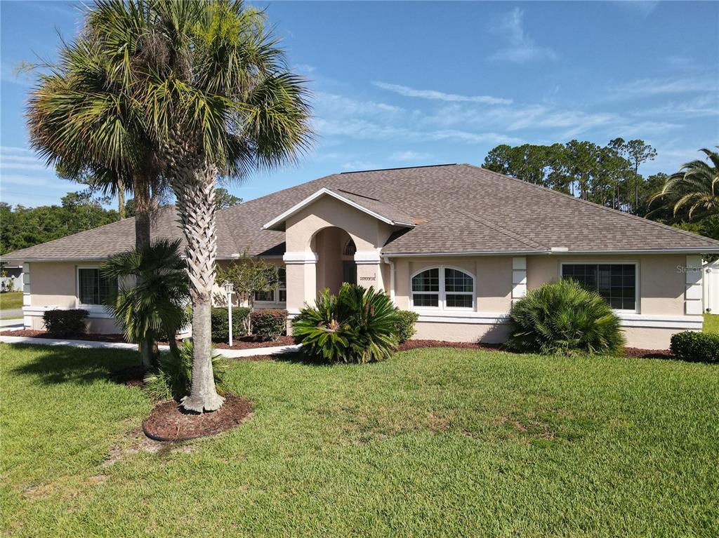 A single-story house with a beige stucco exterior, a hip roof, and a palm tree — 1 EASTMOOR LANE, PALM COAST, FL