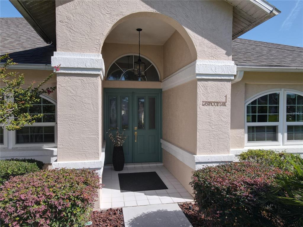 The exterior entrance features a teal double door, arched transom window, and a covered porch — 1 EASTMOOR LANE, PALM COAST, FL