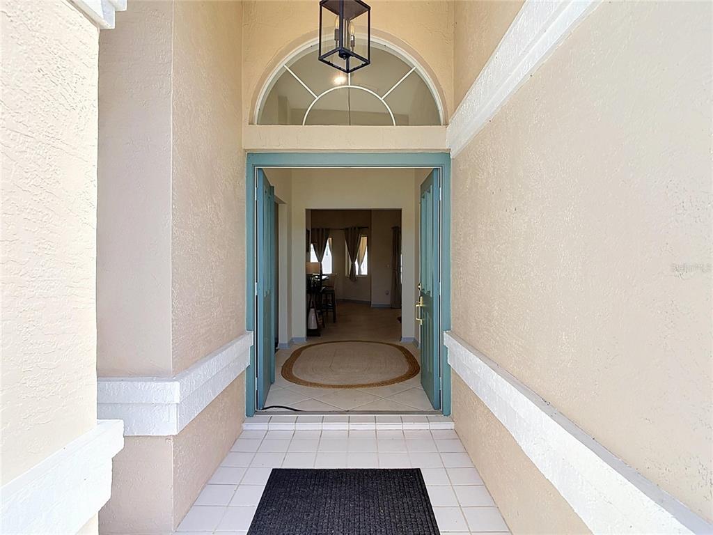 An open front door reveals a tiled entryway with a rug and a hanging lantern — 1 EASTMOOR LANE, PALM COAST, FL
