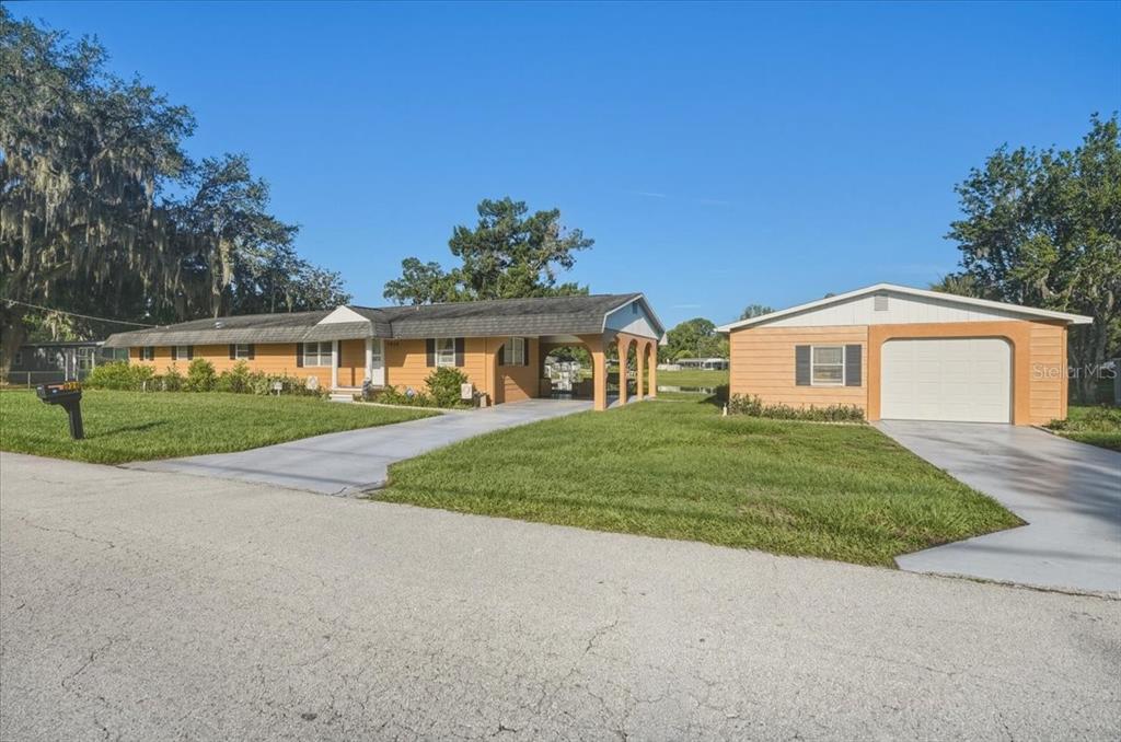 A single-story yellow house with a carport and a detached garage on a grassy lot — 928 S SHAD TERRACE, INVERNESS, FL