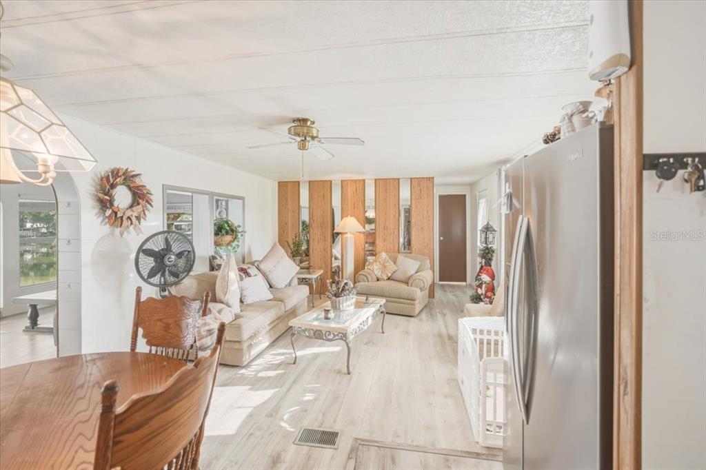 A living room with light wood-look flooring, a ceiling fan, and wood-paneled accent walls — 928 S SHAD TERRACE, INVERNESS, FL