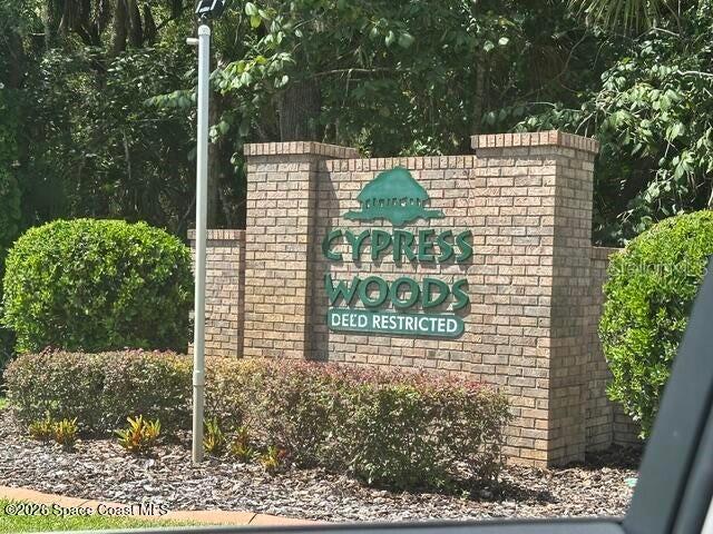 A brick entrance sign for Cypress Woods stands surrounded by green bushes and trees — 7423 BUMELIA DRIVE, COCOA, FL