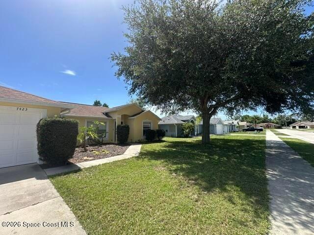 A single-story house with a white garage door and a large tree in the yard — 7423 BUMELIA DRIVE, COCOA, FL