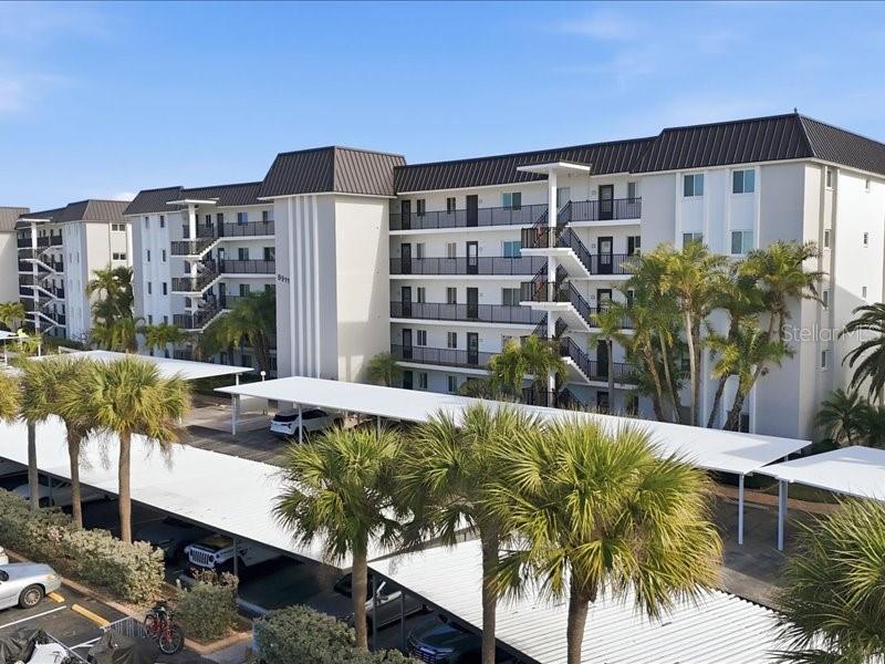 An exterior view of a multi-story apartment building with covered parking and palm trees — 8911 MIDNIGHT PASS ROAD UNIT 208, SARASOTA, FL