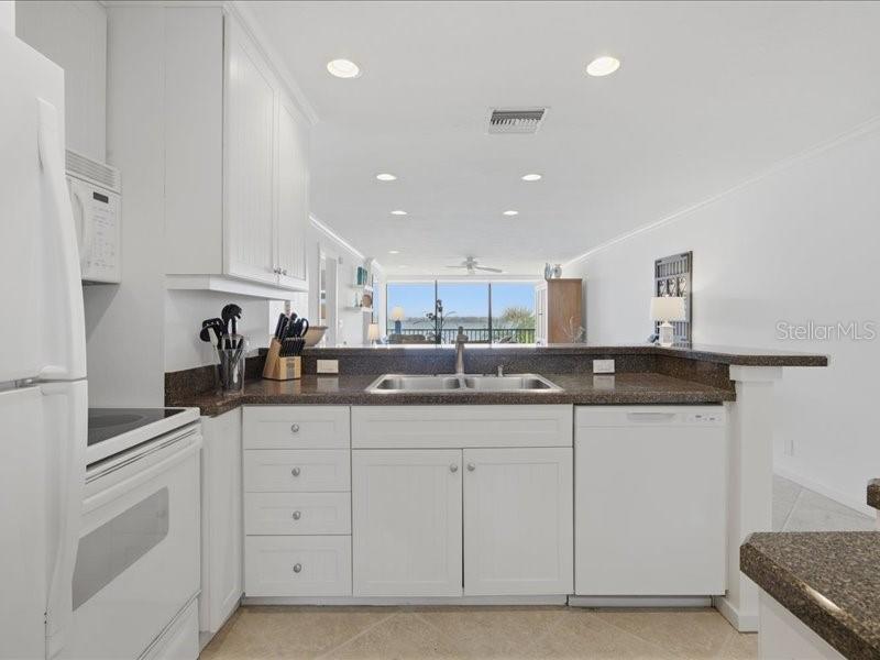 A white kitchen with dark countertops overlooks a living area and a view of water — 8911 MIDNIGHT PASS ROAD UNIT 208, SARASOTA, FL
