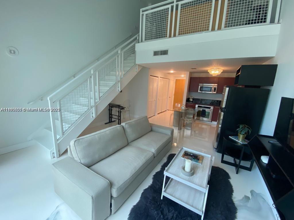 A modern living room features a white sofa, a staircase, and an open kitchen area — 244 Biscayne Blvd # 643, Miami FL 33132, MIAMI, FL