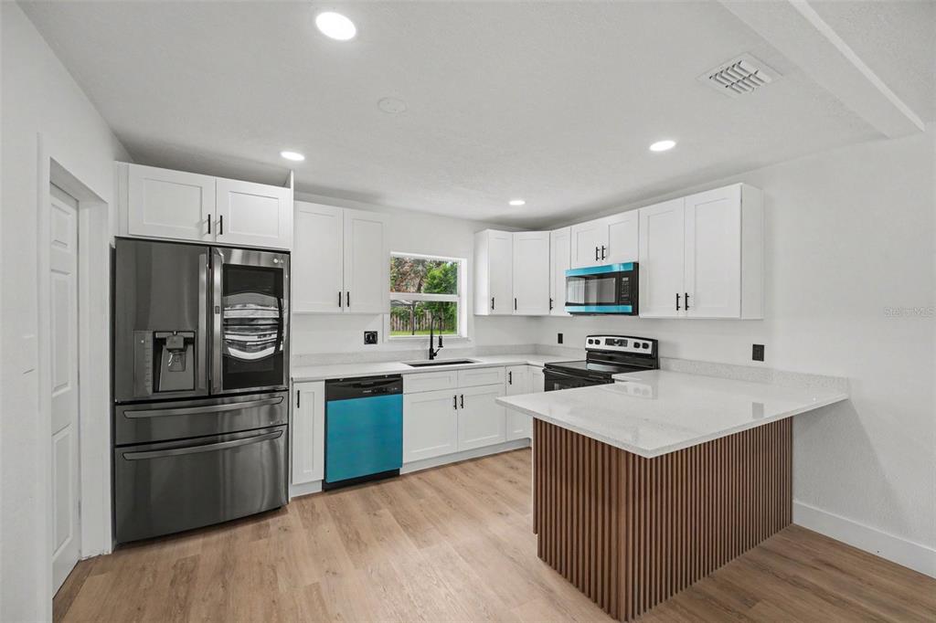 A modern kitchen features white cabinets, stainless steel appliances, a blue dishwasher, and a slatted island — 212 COQUINA DRIVE, COCOA, FL