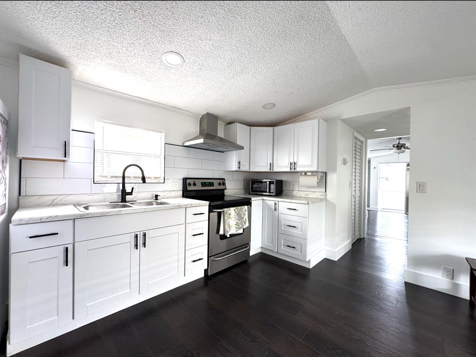 A kitchen with white cabinets, stainless steel appliances, marble-look countertops, and dark wood flooring — 182 Plantation Boulevard, FL 33467, FL