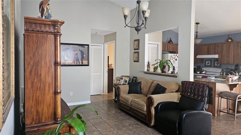 A living room with tile floors, a tan sofa, a black recliner, and an open kitchen — 9906 SURREY RIDGE ROAD, ORLANDO, FL