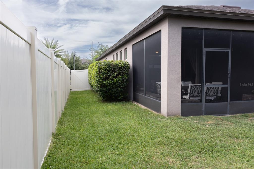 A side yard with a white vinyl fence, green grass, and a screened-in patio — 2892 MATERA DRIVE, ST CLOUD, FL