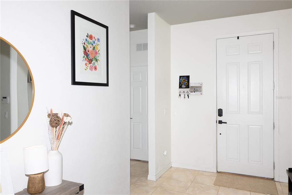A bright entryway features a white door, tiled floors, a round mirror, and wall art — 2892 MATERA DRIVE, ST CLOUD, FL