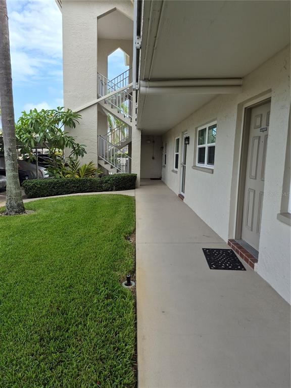 A ground-level concrete walkway runs alongside a building exterior with doors, windows, and stairs — 970 VIRGINIA STREET UNIT 103, DUNEDIN, FL