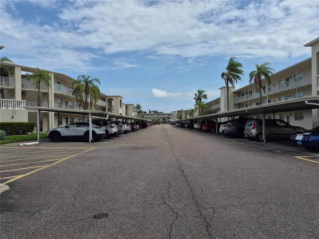 An outdoor parking lot with covered spaces sits between two multi-story apartment buildings — 970 VIRGINIA STREET UNIT 103, DUNEDIN, FL