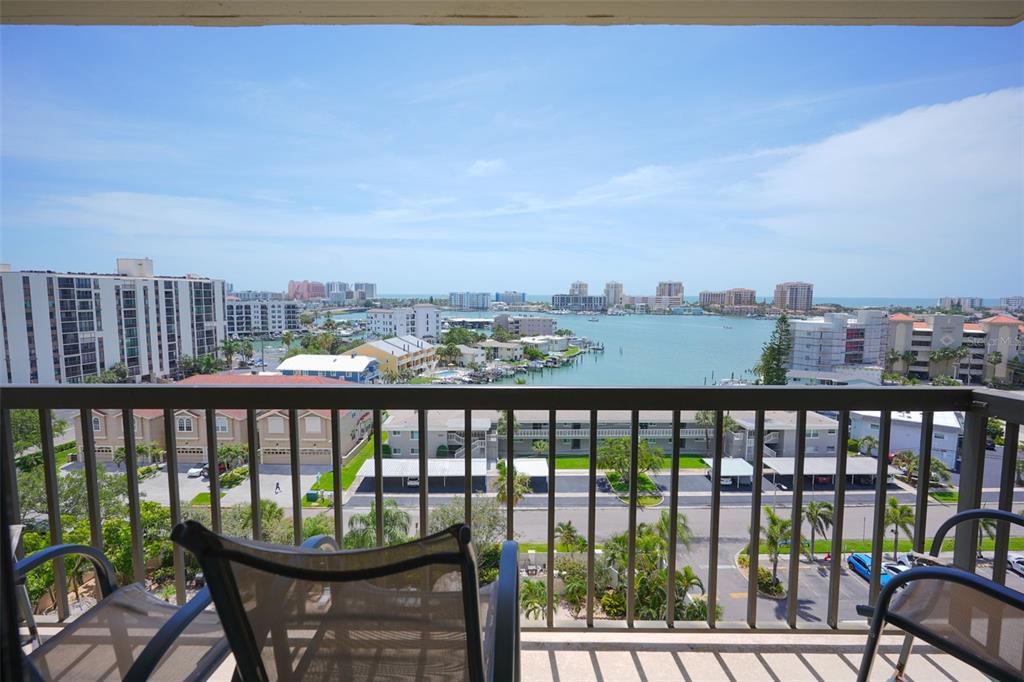 A balcony with a metal railing overlooks a bay, surrounding buildings, and the distant ocean — 400 ISLAND WAY UNIT 1004, CLEARWATER BEACH, FL