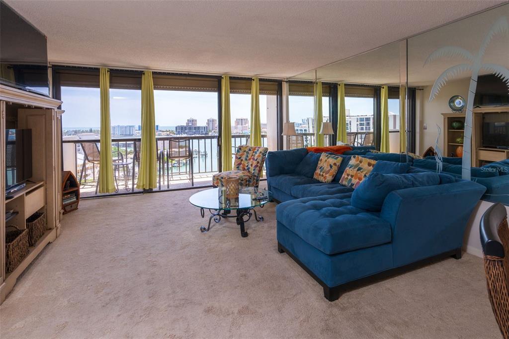 A living room features a blue sectional sofa, a glass coffee table, and a balcony view — 400 ISLAND WAY UNIT 1004, CLEARWATER BEACH, FL