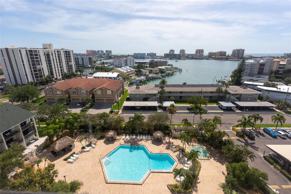 An elevated view of a swimming pool, surrounding buildings, and a bay in the distance — 400 ISLAND WAY UNIT 1004, CLEARWATER BEACH, FL