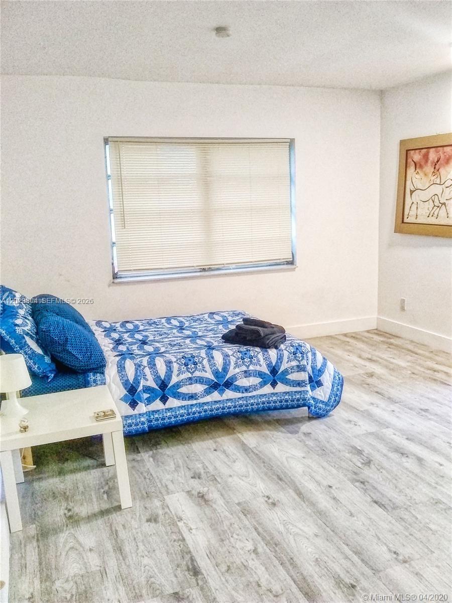 A bedroom features a bed with a blue patterned quilt and light wood-look flooring — 142 NE 56th St # c, Miami FL 33137, MIAMI, FL