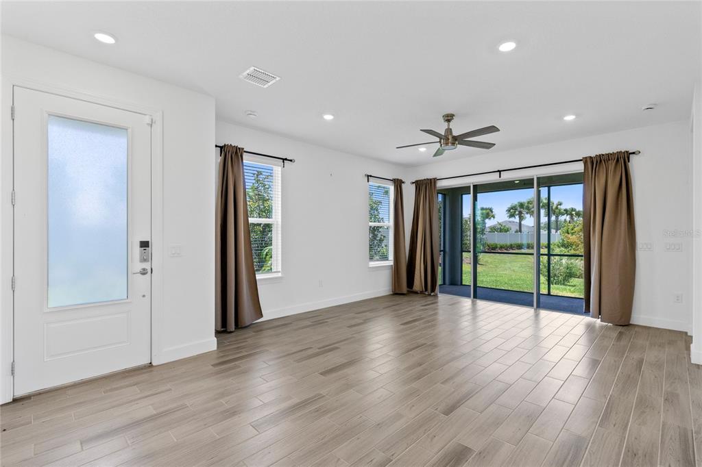 An empty living room with light wood-look tile floors, a ceiling fan, and sliding glass doors — 5338 SPOONFLOWER COURT, ST CLOUD, FL