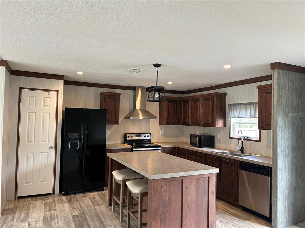 A kitchen features dark wood cabinetry, a central island with stools, and black appliances — 11231 NE 60TH STREET, BRONSON, FL
