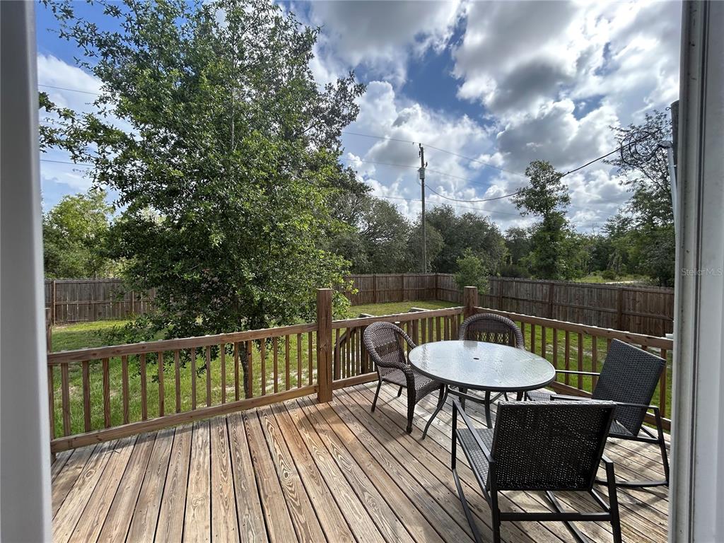 A wooden deck features a patio table and chairs overlooking a fenced backyard — 11231 NE 60TH STREET, BRONSON, FL
