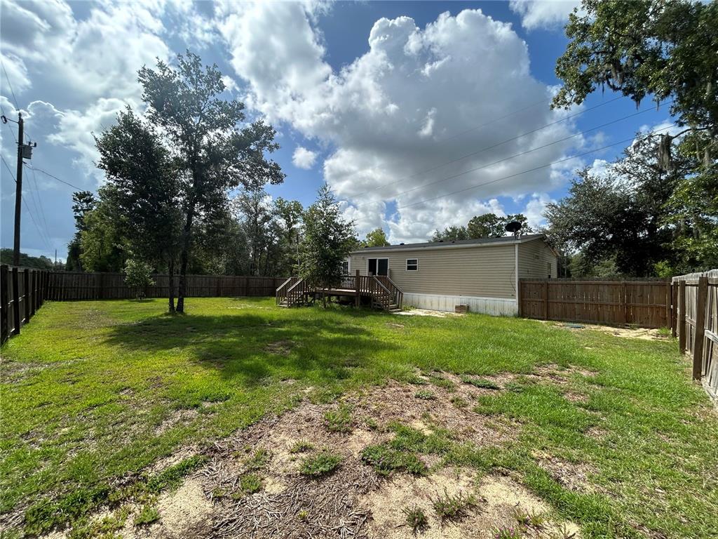 A backyard with a wooden deck attached to a tan mobile home and wooden fencing — 11231 NE 60TH STREET, BRONSON, FL