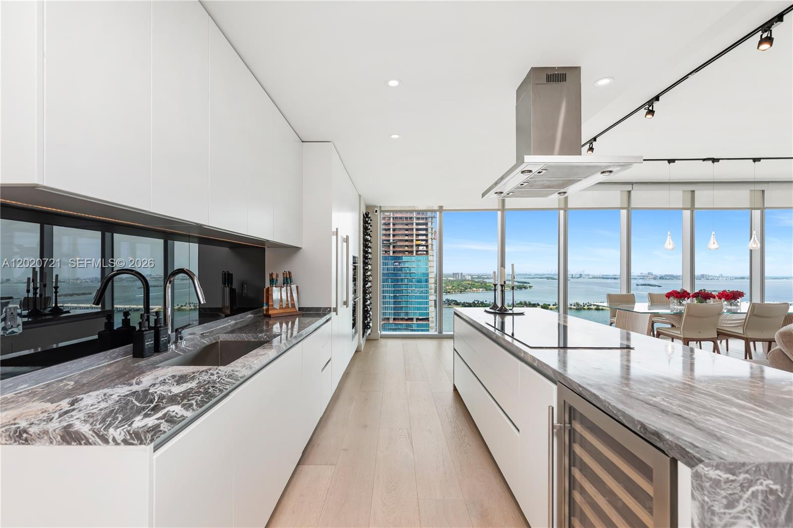 A modern kitchen features white cabinetry, marble countertops, a large island, and floor-to-ceiling windows — 700 NE 26th Ter # 2901, Miami FL 33137, MIAMI, FL