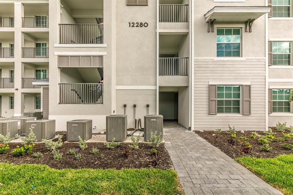 Exterior view of a multi-story apartment building with air conditioning units and a paved walkway — 12280 WELLEN GOLF STREET UNIT 403, VENICE, FL