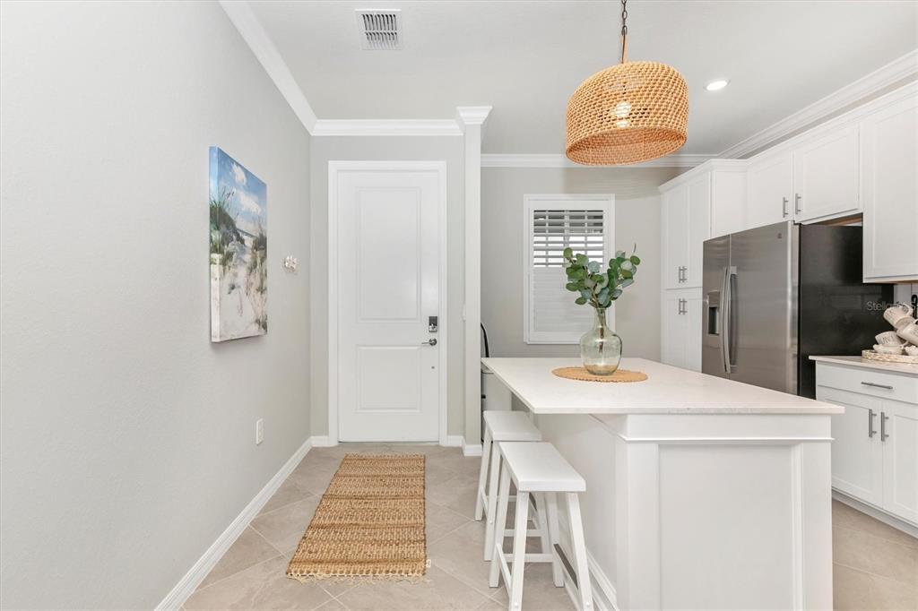 A kitchen features white cabinetry, a central island with bar stools, and a woven pendant light — 12280 WELLEN GOLF STREET UNIT 403, VENICE, FL