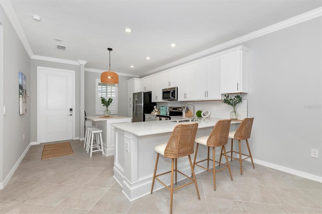 A bright kitchen features white cabinetry, a large island with bar seating, and tile flooring — 12280 WELLEN GOLF STREET UNIT 403, VENICE, FL