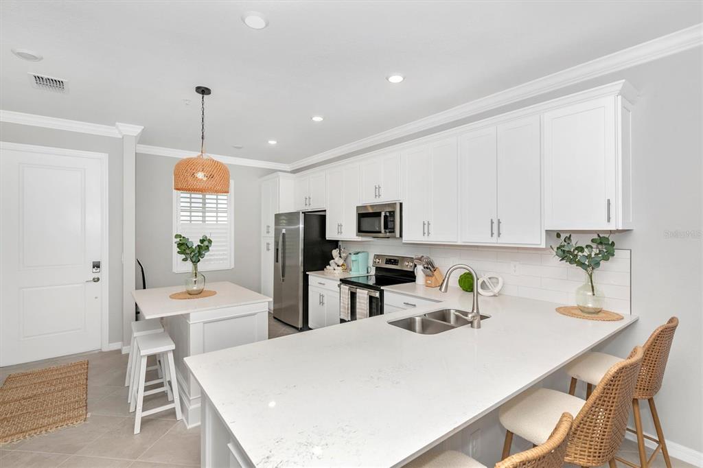 A modern kitchen features white cabinetry, quartz countertops, a kitchen island, and stainless steel appliances — 12280 WELLEN GOLF STREET UNIT 403, VENICE, FL