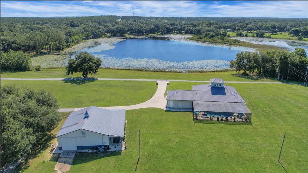 An aerial view shows a house with a pool enclosure, a detached garage, and a lake — 16982 SE HIGHWAY 42, WEIRSDALE, FL