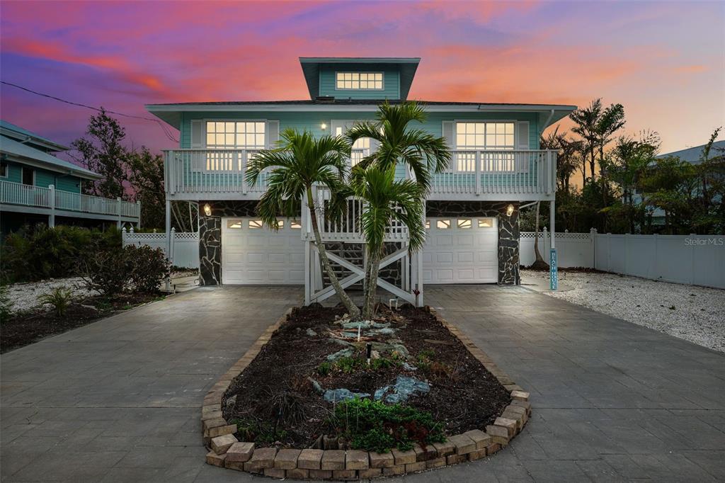 A two-story elevated beach house with a paved driveway, palm trees, and a sunset sky — 311 POINSETTIA ROAD, ANNA MARIA, FL