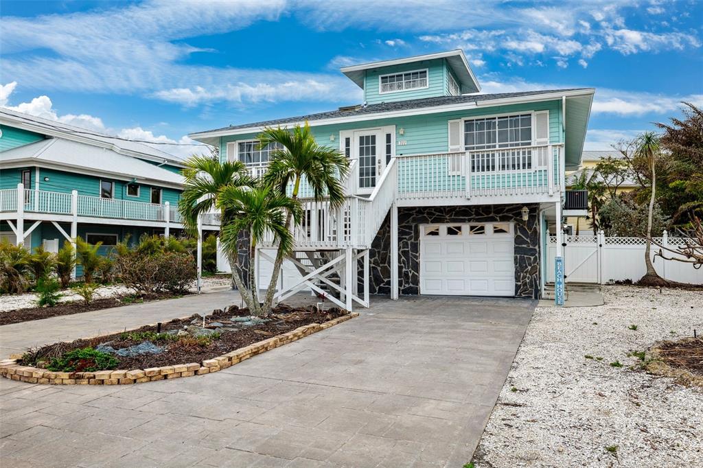 A light blue elevated house features a white staircase, a garage, and a palm tree — 311 POINSETTIA ROAD, ANNA MARIA, FL