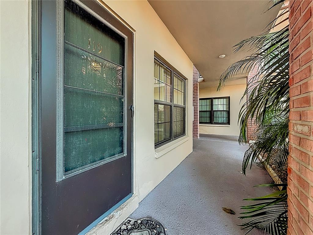 A covered outdoor walkway leads to a front door numbered 119 with a screen door — 1020 85TH AVENUE N UNIT 119, ST PETERSBURG, FL