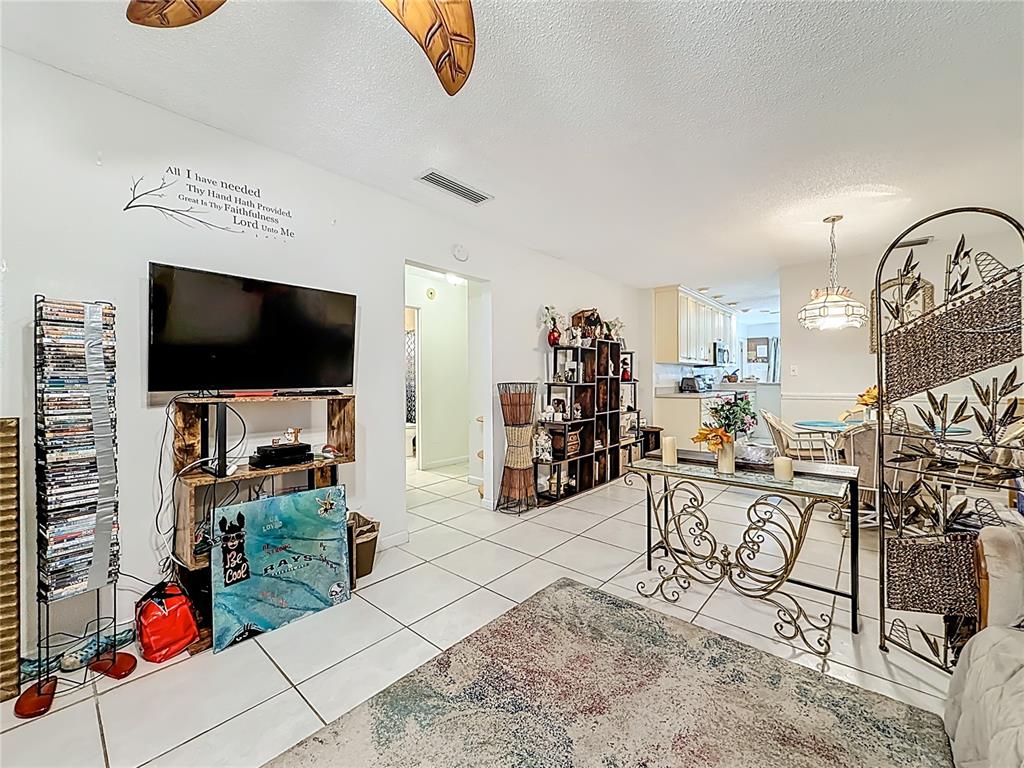 A living room with tile floors, a television on a wooden stand, and a dining area — 1020 85TH AVENUE N UNIT 119, ST PETERSBURG, FL