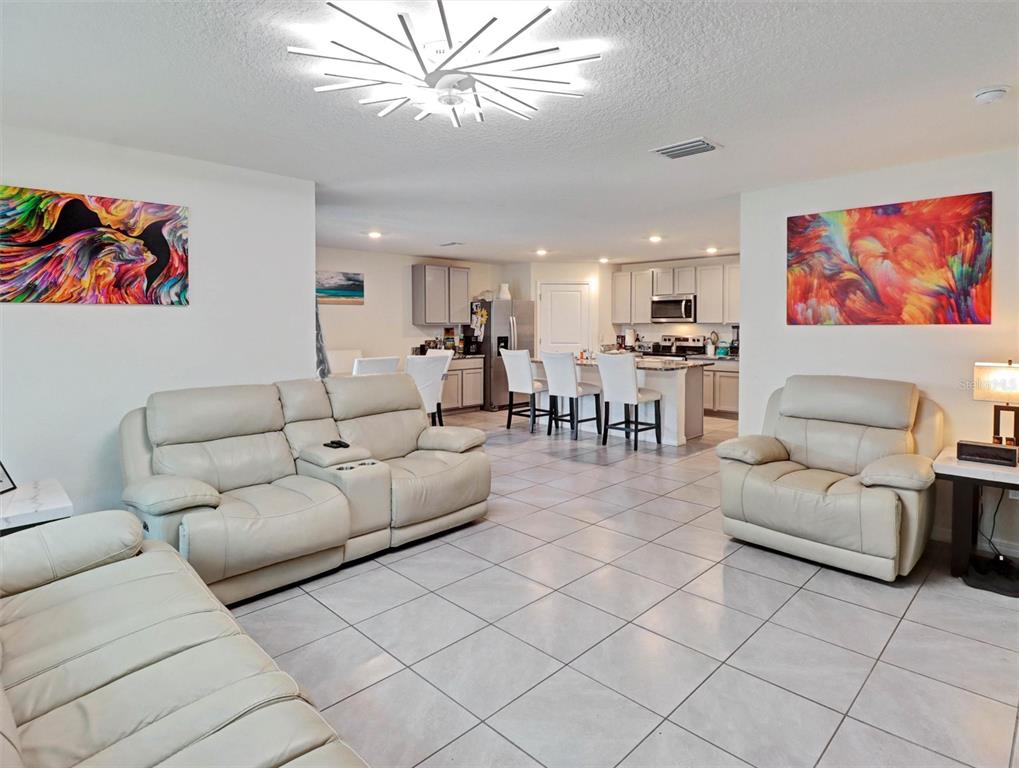 A living room with light-colored leather furniture, tile flooring, and a kitchen in the background — 1202 TAHITIAN SUNRISE DRIVE, PLANT CITY, FL