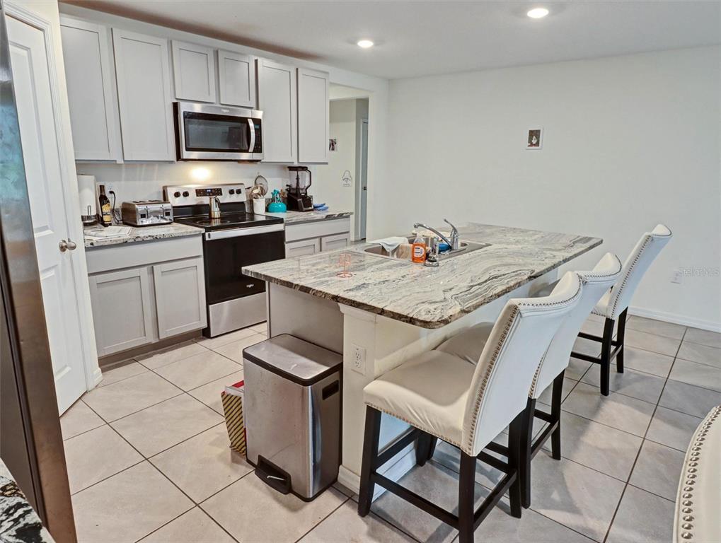 A kitchen features light gray cabinets, granite countertops, a central island, and three bar stools — 1202 TAHITIAN SUNRISE DRIVE, PLANT CITY, FL