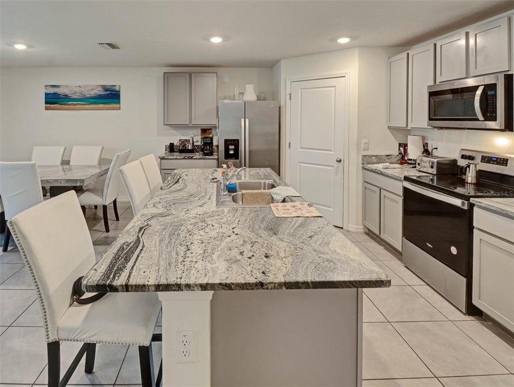 A kitchen features a large granite-topped island, stainless steel appliances, and light gray cabinetry — 1202 TAHITIAN SUNRISE DRIVE, PLANT CITY, FL