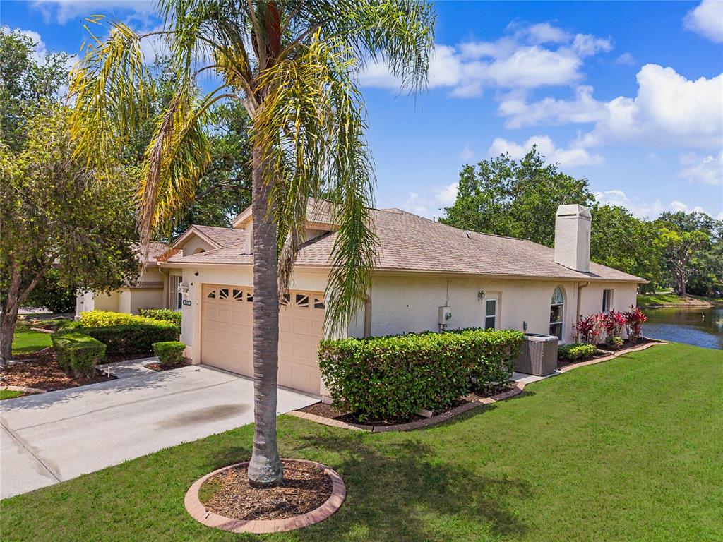 A single-story house with a two-car garage and a chimney sits beside a pond — 5657 29TH STREET CIRCLE E, BRADENTON, FL