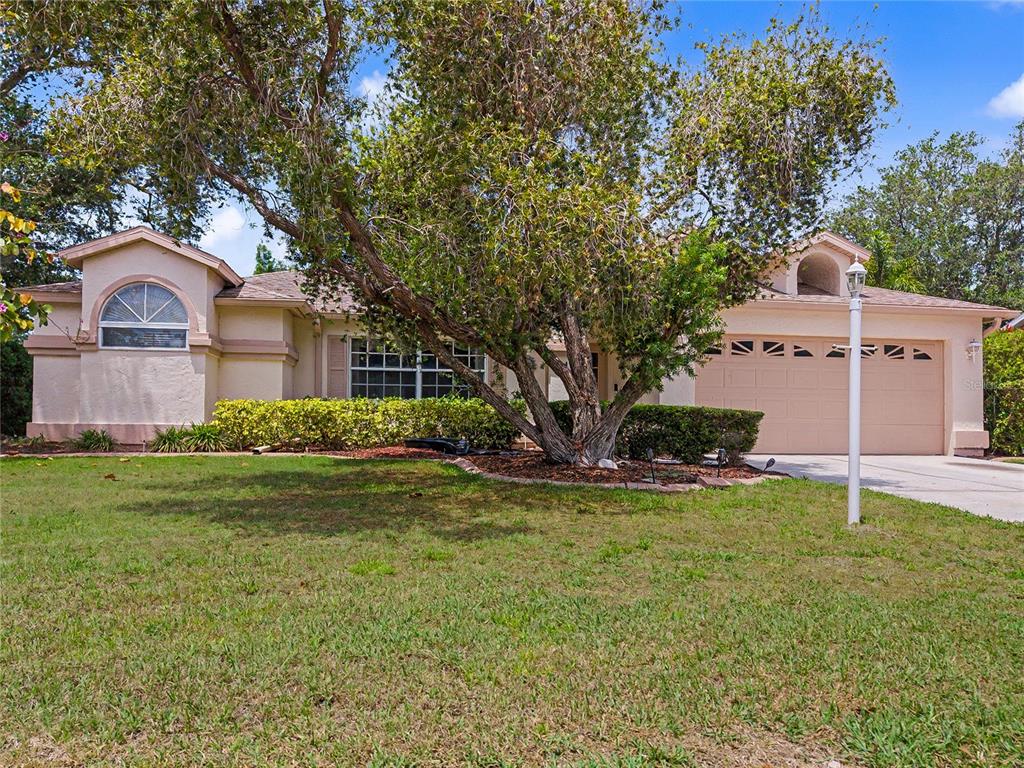 A single-story house with a tan stucco exterior, a two-car garage, and a large tree — 5657 29TH STREET CIRCLE E, BRADENTON, FL