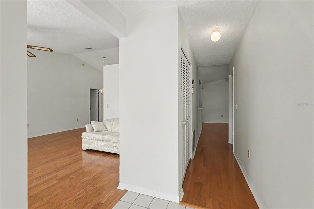 A hallway with hardwood floors leads past a closet toward a living room area — 5657 29TH STREET CIRCLE E, BRADENTON, FL