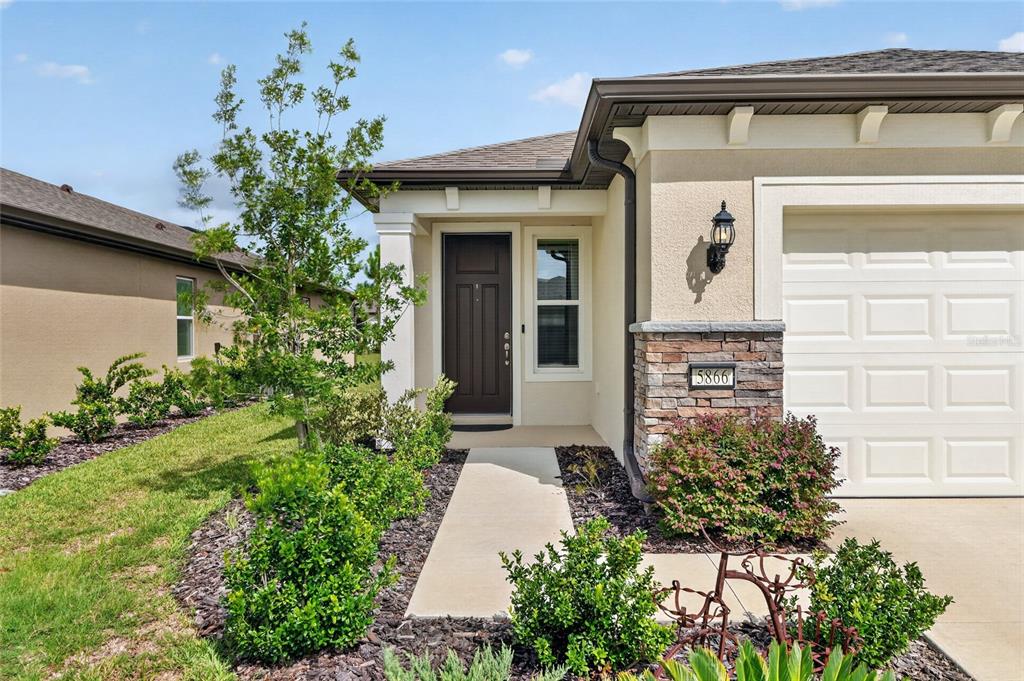 The exterior of a house features a dark front door, stone accents, and landscaping — 5866 SW 87TH AVENUE, OCALA, FL