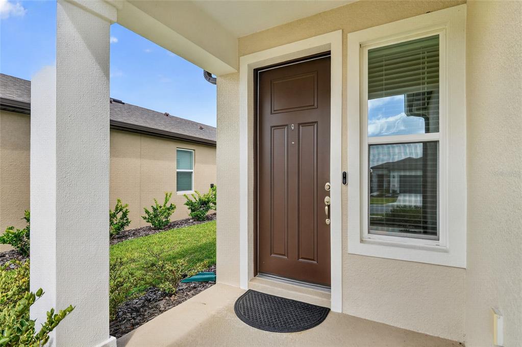 A brown front door with a side window and a small mat on a porch — 5866 SW 87TH AVENUE, OCALA, FL
