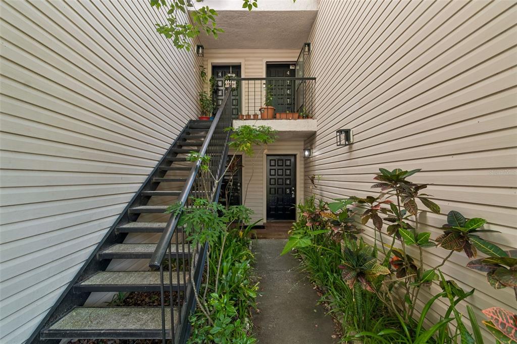 An outdoor staircase leads to an upper balcony with two doors above a ground-level entrance — 4745 PURITAN CIRCLE UNIT 4745, TAMPA, FL